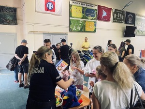Policjantka przy stoisku wręcza dzieciom kolorowanki.