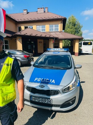Policjant obok radiowozu policyjnego, w tle szkoła.