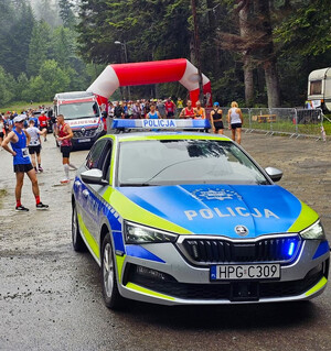 oznakowany radiowóz w pobliżu startu jednego z biegów, w tle zawodnicy
