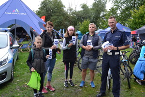 Policjant oraz uczestnicy pikniku trzymają w ręku ulotki