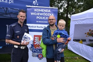 Policjant trzyma w ręku ulotkę obok mężczyzna trzyma na rękach dziecko