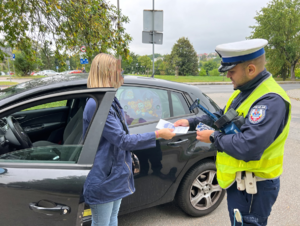 umundurowany policjant wręcza naklejkę kierowcy w ramach kampanii Mistrzu Zwolnij