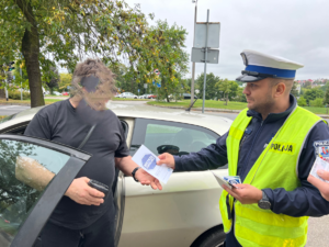 umundurowany policjant wręcza ulotkę kierowcy w ramach kampanii Mistrzu Zwolnij