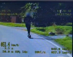 Zdjęcie  z wideorejestratora, na którym widać chłopaka jadącego po drodze na hulajnodze elektrycznej i zarejestrowaną prędkość 51 kilometrów na godzinę