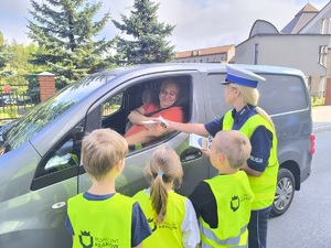 Policjantka z dziećmi rozdają ulotki kierowcy.