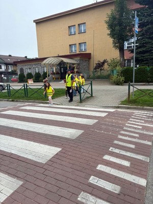 Dziecko przechodzą ce przez przejscie dla pieszych  a obok stojacy policjant