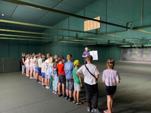 Policjanct wraz z grupą dzieci znajduje się na strzelnicy Komendy Powiatowej Policji w Chrzanowie.