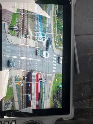 Widok z policyjnego drona. Przejazd kolejowy w Rzezawie. Na zdjęciu widoczny pociąg oraz samochody stojące przed zamkniętym szlabanem