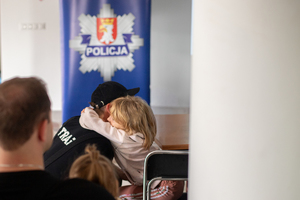 dziecko przytula stażaka, w tle logo komendy powiatowej