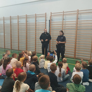 umundurowana policjantka i policjant przed nimi siedzą dzieci podczas pogadanki na sali gimnastycznej