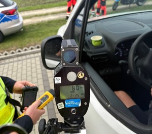 Kampania Mistrzu zwolnij i Road Safety Days policjant z miernikiem i alkoblow  przy samochodzie