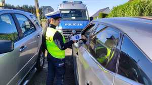 Kampania Mistrzu zwolnij i Road Safety Days  policjantka wręcza ulotkę kierowcy w tle radiowóz