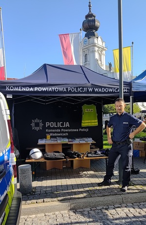 Namiot z napisem Komenda Powiatowa Policji w Wadowicach, w którym na stoliku poukładany jest sprzęt policyjny i materiały edukacyjne. Po prawej policjant.