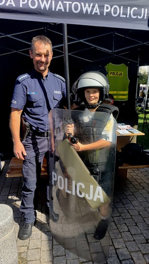 Policjant i chłopiec, ubrany w elementy wyposażenia policyjnego.