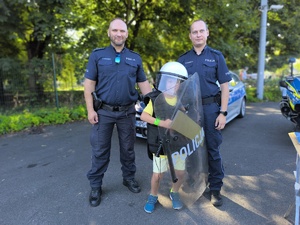 dziecko ubrane w elenenty policyjnego umundurowania pozuje do zdjęcia z dwoma policjantami