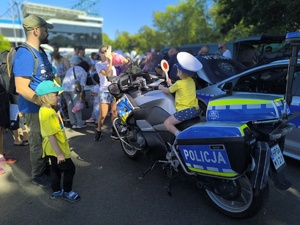 dziecko w policyjnej czapce siedzi na policyjnym motocyklu, wokół uczestnicy wydarzenia