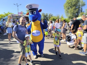 mężczyzna z dzieckiem pozują do zdjęcia z maskotką krakowskiej Policji