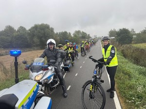 Policjant na motocyklu i polcijantka na rowerze w tle dzieci na rowerach