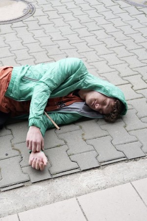 Młody meżczyzna leżacy na kostke brukowej z piersi wystaje mu metalowy pret