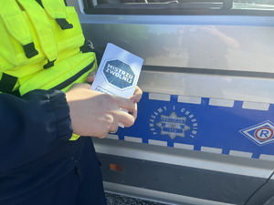 policjant trzymający w ręce ulokę mistrzu zwolnij, w tle fragment policyjnego radwiozu