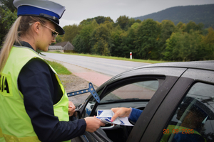 umundurowana policjantka rozdająca ulotki informacyjne podczas kontroli drogowej