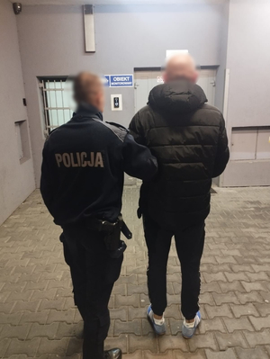 policjant prowadzi mężczyznę do pomieszczenia dla osób zatrzymanych