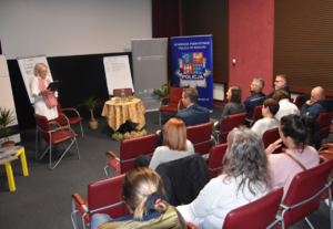 Banery Starostwa Powiatowego w Bochni oraz Komendy Powiatowej Policji w Bochni. Starosta Bocheński, umundurowany policjant oraz uczestnicy i prowadząca spotkanie