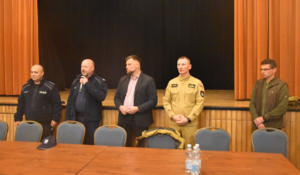 Umundurowani policjanci oraz strażacy. Na zdjęciu Komendant Powiatowy Policji w Bochni z mikrofonem w ręku