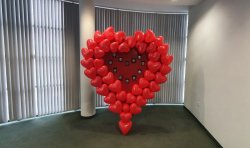 wielkie serce zrobione z czerwonych balonów stoi w pomieszczeniu komisariatu, wewnątrz serca przypięte odznaki policyjne