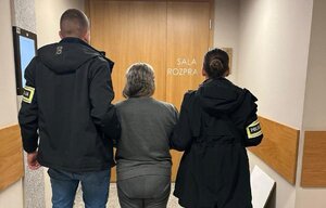 Kobieta oszukujaca na legendę prowadzona na salę rozpraw przez policjantów operacyjnych