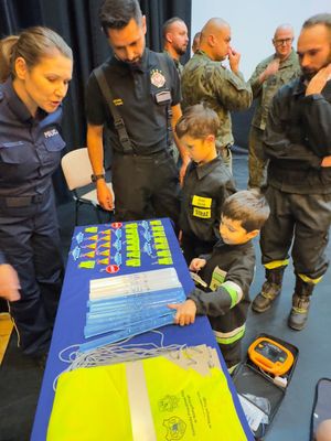 pOLICJANTKA I DZIECI STOJACE OBOK STOLIKA Z ODBLASAKAMI