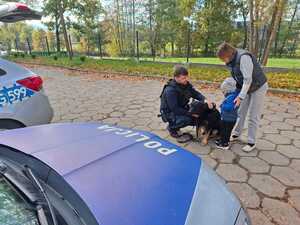 dziecko głaszczące policyjnego psa w towarzystwie kobiety i policjanta