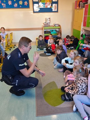 Policjant mwoiacy do dzieci siedzących na dywanie