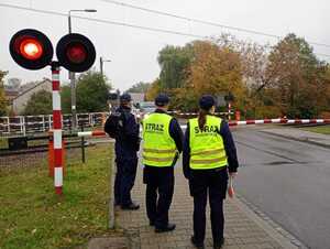 Policjant i funkcjonariusze SOK patrzą na zamknięty przejazd kolejowy