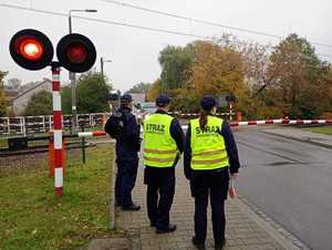 Policjant i funkcjonariusze SOK patrzą na zamknięty przejazd kolejowy