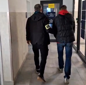 nieumundurowany policjant prowadzi zatrzymanego przez korytarz komisariatu