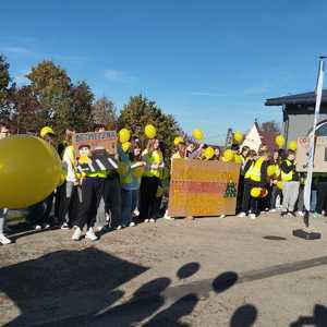 uczniowie w kamizelkach odblaskowych z banerem i balonami