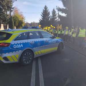 oznakowany radiowóz obok dzieci idące w kamizelkach odblaskowych