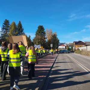 oznakowany radiowóz zabezpiecza przemarsz uczniów ubranych w kamizelki odblaskowe