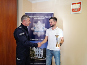 Komendant gratuluje policjantowi pionu kryminalnego, który trzyma puchar w ręce