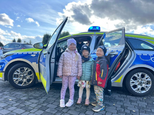 dzieci stojące przed oznakowanym radiowozem