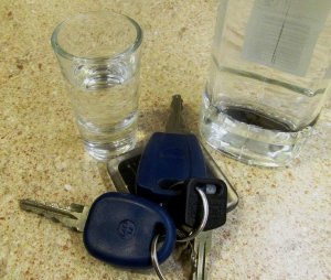 kluczyki do pojazdu, obok butelka i kieliszek z alkoholem