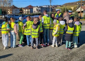 Grupa dzieci w kamizelkach odblaskowych i dwóch policjantów ruchu drogowego