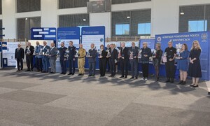 Przedstawiciele służb mundurowych, władz samorządowych, szkoły, którzy stoją obok siebie. w Tle banery.