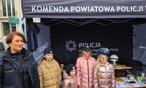 Policjantka i cztery dziewczynki, które mają założone policyjne czapki. W tle policyjny namiot.