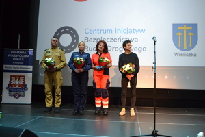 Strażak, policjantka, pielęgniarka i Jakub uczestnik wypadku stoją na scenie trzymając w ręku kwiaty