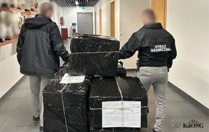 Dwóch funkcjonariuszy Straży Granicznej w korytarzu, oglądających stos dużych paczek owiniętych czarną folią, przewiązanych sznurkiem, z dokumentami przewozowymi na wierzchu.
