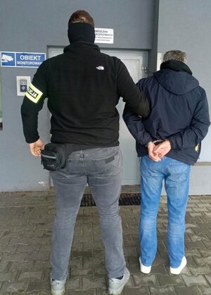 nieumundurowany policjant trzyma za rekę mężczyznę przed wejście do pomieszczenia dla osób zatrzymanaych