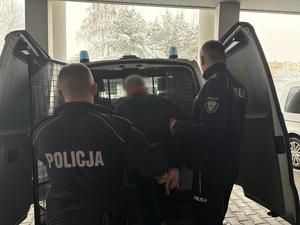 Policjanci prowadzą zatrzymanego do radiowozu