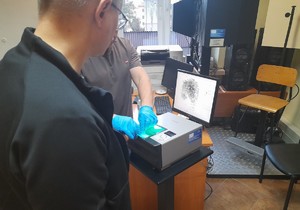 Technik kryminalistyki prezentuje aktorowi skanowanie odcisków